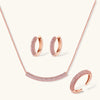 Rose gold pavé zirconia bar necklace, hoop earrings, and open ring set with pink stones on cream background.