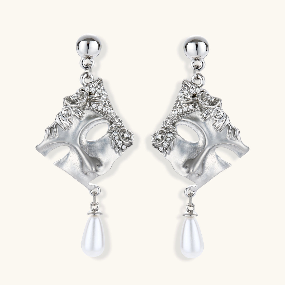 Ornate silver-toned theatrical mask earrings with crystal details and pearl drops on white background.