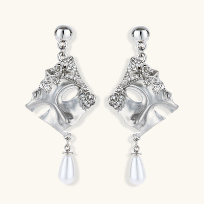 Ornate silver-toned theatrical mask earrings with crystal details and pearl drops on white background.