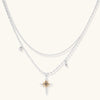 Two-layer silver-toned necklace with star charms and dagger pendant featuring golden sun motif on white background.