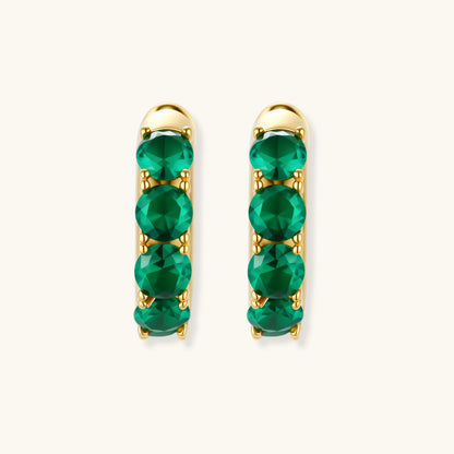 Close-up of gold-plated huggie hoop earrings featuring four emerald green cubic zirconia stones on white background.