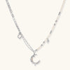Silver-toned crescent moon pendant with star accents on pearl and chain necklace against white background.