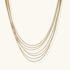 Seven delicate gold-plated snake chains create an elegant layered necklace on a neutral background.