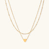Delicate double-chain gold necklace with tiny heart pendant on cream background