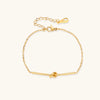 Delicate gold chain bracelet with minimalist bar and centered knot detail on cream background