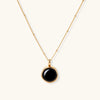 Circular black agate pendant on gold-plated sterling silver chain against cream background, showing modern minimalist design.
