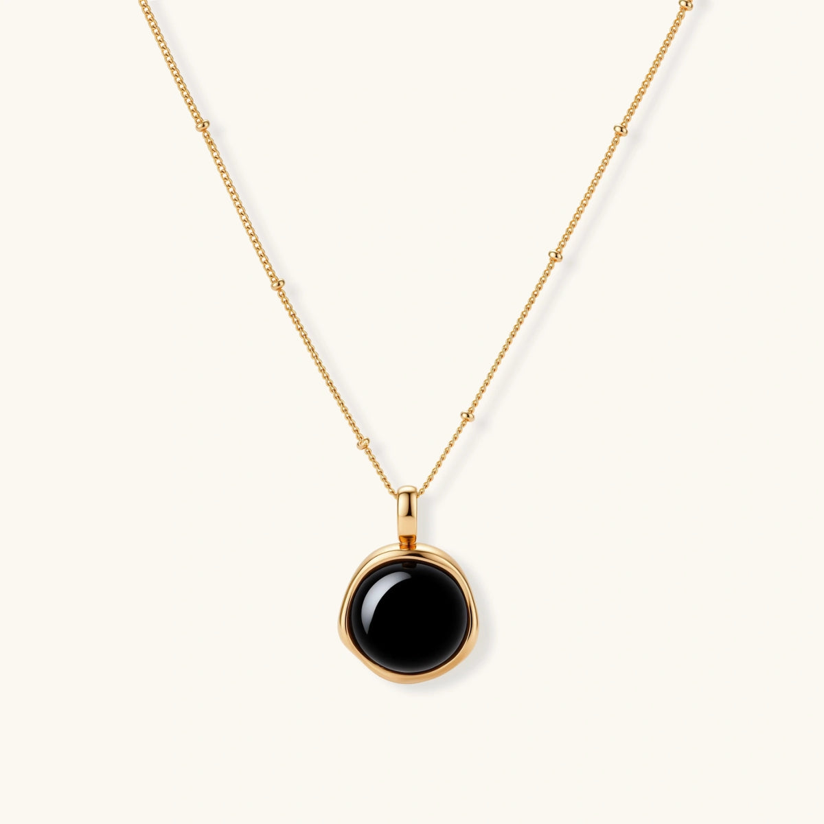 Circular black agate pendant on gold-plated sterling silver chain against cream background, showing modern minimalist design.