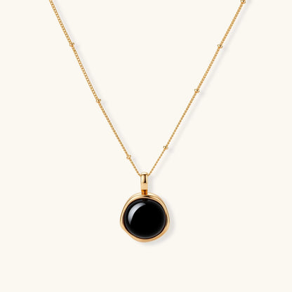Circular black agate pendant on gold-plated sterling silver chain against cream background, showing modern minimalist design.