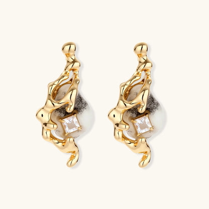 Close-up of metallic dragon-wrapped earrings with marbled resin stones on white background