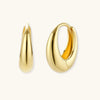 Chunky gold-plated sterling silver huggie hoop earrings with hinged closure mechanism on cream background.