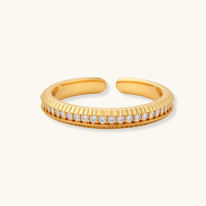 Adjustable gold-plated ring with row of sparkling crystals on ribbed band, shot against cream background