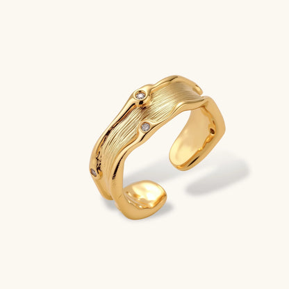Gold-plated sculptural ring with flowing wave texture and two round zirconia stones in adjustable cuff design