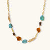 Statement necklace with gold chain, turquoise stones, amber beads, and wooden elements on cream background.