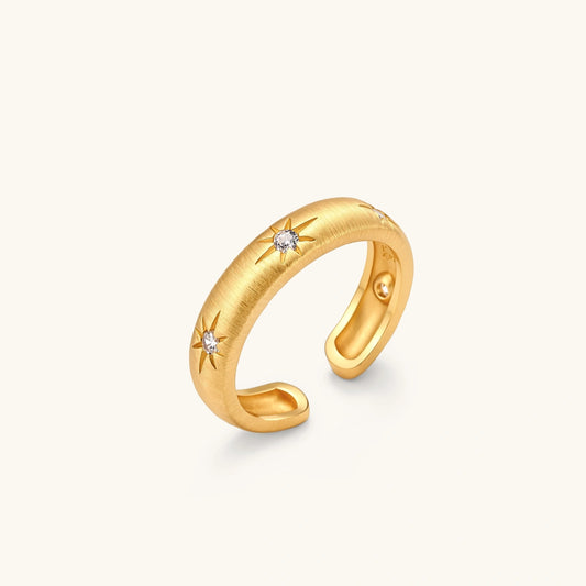 Gold open-band cuff ring with brushed matte finish, engraved 8-point star motifs, and round CZ stones on white background.